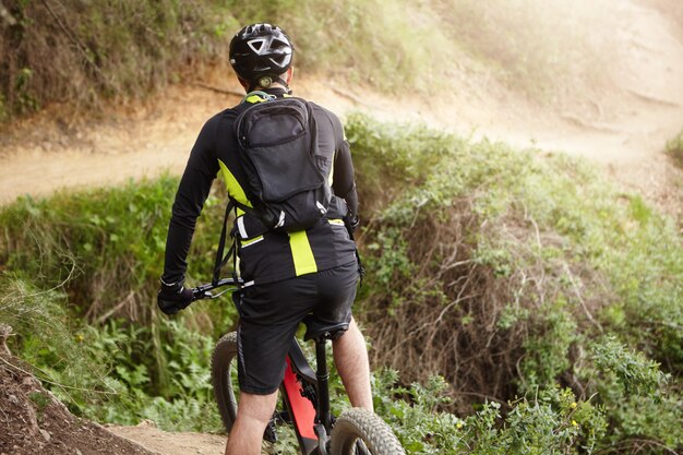 Achteraanzicht van fietser in zwarte kleding elektrische fiets rijden in heuvelachtig landelijk gebied