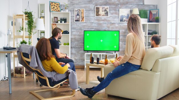 Achteraanzicht van goede vrienden met handen in de lucht tijdens het kijken naar een voetbalwedstrijd in de woonkamer.