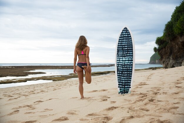 Achteraanzicht van jonge vrouwelijke surfer stretching leg