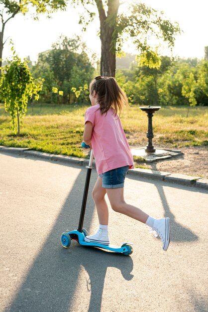 Achteraanzicht van meisje met roze t-shirt op scooter