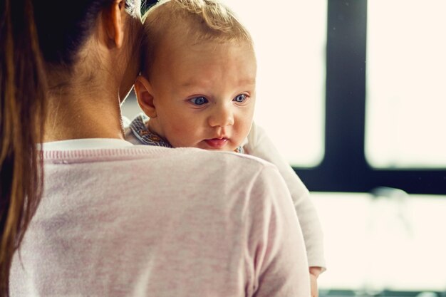 Gratis foto achteraanzicht van moeder die haar zoontje thuis vasthoudt focus ligt op baby