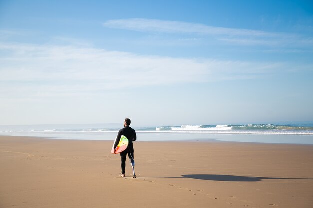 Achteraanzicht van surfer staande op zandstrand met bord