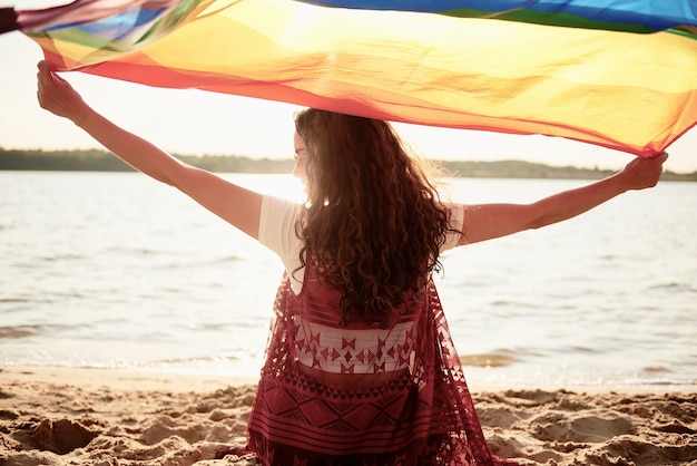 Achteraanzicht van vrouw met regenboogvlag op het strand