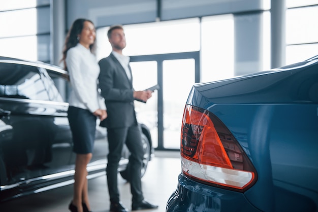 Achterkant van de blauw geschilderde auto. Vrouwelijke klant en moderne stijlvolle bebaarde zakenman in de auto-salon