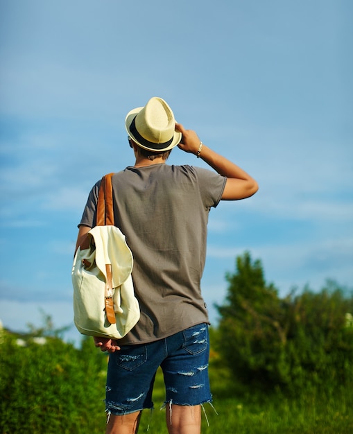 achterkant van jonge aantrekkelijke moderne stijlvolle man in casual doek in hoed in glazen achter blauwe hemel