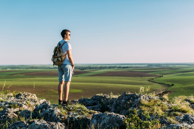 Achtermening van de jonge mens die zich bovenop rots bevindt die groen landschap bekijkt