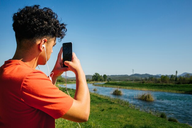 Achtermening van de mens met oortelefoon die beeld op smartphone nemen