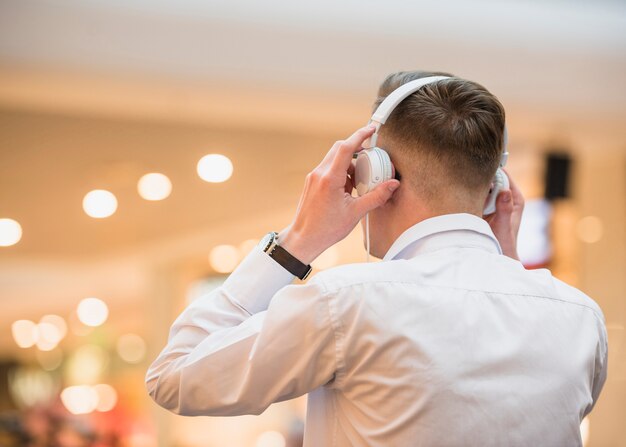 Achtermening van een jonge mens het luisteren muziek op witte hoofdtelefoon