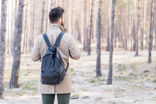 Achtermening van een mannelijke reiziger met zijn rugzak die in het bos kijken