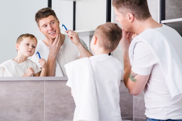 Achtermening van een vader en een zoon die in de spiegel scheermes in hand houden