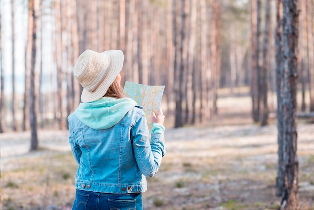 Achtermening van een vrouw die hoed dragen die kaart in het bos bekijken