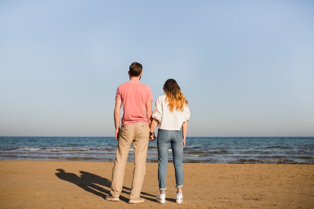 Achtermening van jong paar die elkaars hand houden kijkend op zee