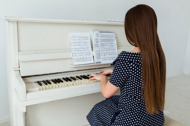 Achtermening van jonge vrouw met lange haar het spelen piano