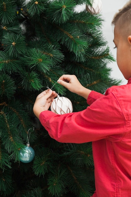 Achtermening van jongen die Kerstmisboom verfraait