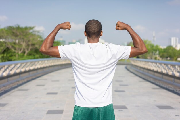 Achtermening van sportieve zwarte kerel die en beide bicepsen stellen buigen.