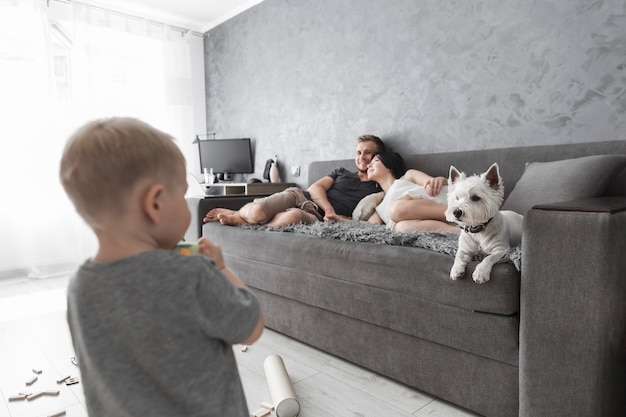 Achtermening van weinig jongen die zijn ouder het ontspannen op bank met hond bekijken