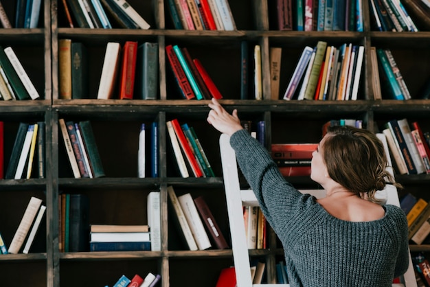 Achtermeningsvrouw die boek van plank kiezen