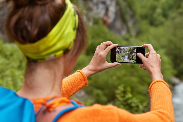 Achterwaarts schot van vrouw toerist maakt foto van rivier in ravijn op smartphoneapparaat voor posten in sociale netwerken