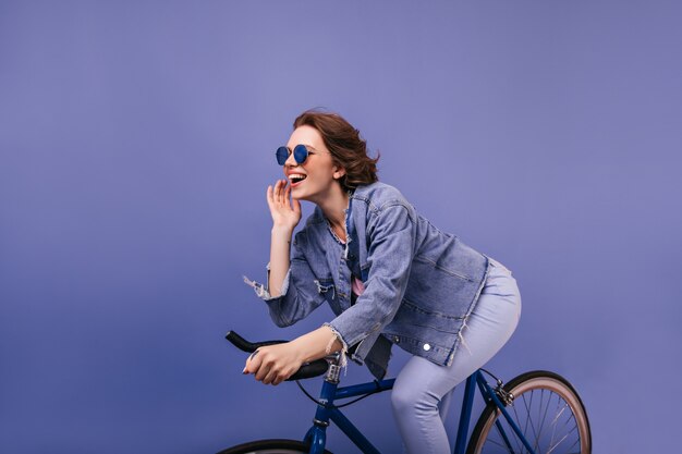 Actief donkerbruin meisje dat op fiets berijdt. Indoor foto van vrolijke dame in denim jasje zittend op de fiets.