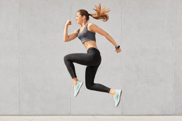 Actieve vrouw die vol energie is, hoog in de lucht springt, sportkleding draagt, zich voorbereidt op sportwedstrijden