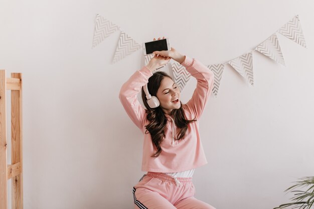 Actieve vrouw in roze pak is dansen in haar appartement en luisteren naar muziek op de koptelefoon