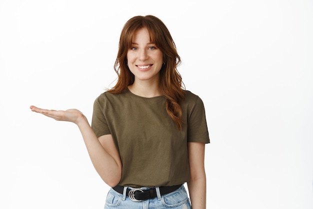 Advertentie- en winkelconcept Glimlachende vrouw die iets in de open hand houdt, strekt de palm uit en ziet er gelukkig uit met een product dat op een witte achtergrond staat