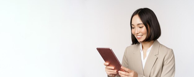 Afbeelding van een Aziatische zakenvrouw die een digitale tablet gebruikt die naar een gadget kijkt en glimlacht terwijl ze staand werkt