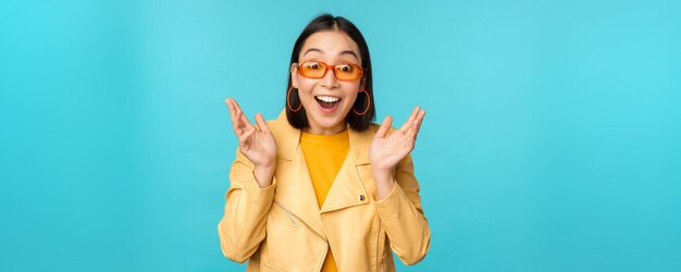 Afbeelding van een enthousiaste jonge aziatische vrouw die triomfantelijk viert en er verrast en blij uitziet, tevreden handen klappend over een blauwe achtergrond