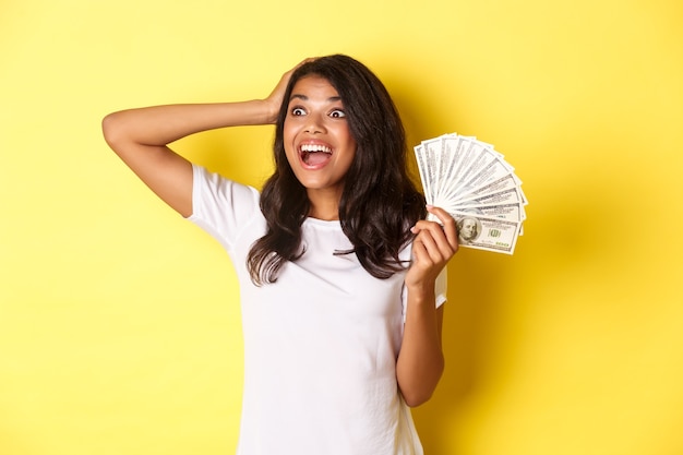 Afbeelding van een gelukkig Afrikaans-Amerikaans meisje dat opgewonden kijkt in de linkerbovenhoek en geld vasthoudt