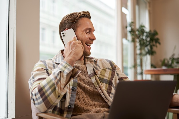 Afbeelding van een gelukkige café bezoeker man met een laptop die een vriend belt over de telefoon zakenman die aan het praten is