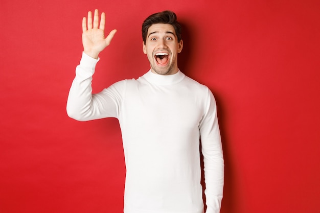 Afbeelding van een gelukkige en vriendelijke jongeman die hallo zegt met de hand zwaaiend om iemand te begroeten die over een rode ba...