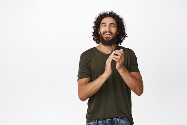 Afbeelding van een gelukkige jonge man die lacht en applaudisseert in zijn handen en er trots uitziet en je complimenteert terwijl hij op een witte achtergrond staat