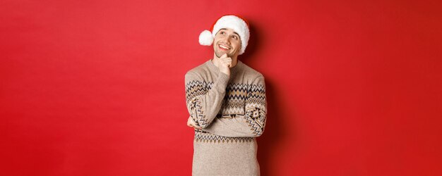 Afbeelding van een gelukkige jonge man met een kerstmuts en een kersttrui die iets voorstelt dat aan het nieuwe ja denkt...