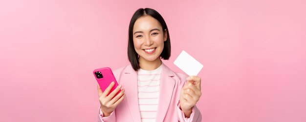Afbeelding van een glimlachende, gelukkige Aziatische zakenvrouw die creditcard toont die online betaalt op smartphone-applicati