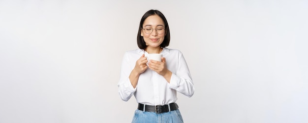 Afbeelding van een glimlachende Koreaanse vrouw die geurkoffie snuift in een mok en geniet van een heerlijk drankje dat over de