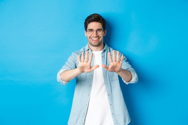 Afbeelding van een glimlachende man die tevreden naar zijn manicure kijkt, een schoonheidssalon bezoekt en over een blauwe achtergrond staat