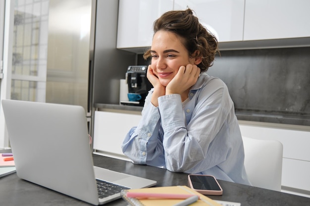 Gratis foto afbeelding van een glimlachende vrouw die op afstand studeert en naar een laptop kijkt terwijl ze thuis naar een webinar kijkt