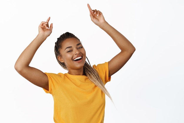 Afbeelding van een glimlachende zwarte vrouw die met haar vingers omhoog wijst en een grote reclame voor de verkoop van promo's toont met een gele t-shirt op een witte achtergrond