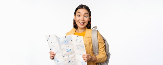 Afbeelding van een jonge Aziatische meisje toeristische reiziger met kaart en rugzak poseren tegen witte studio background