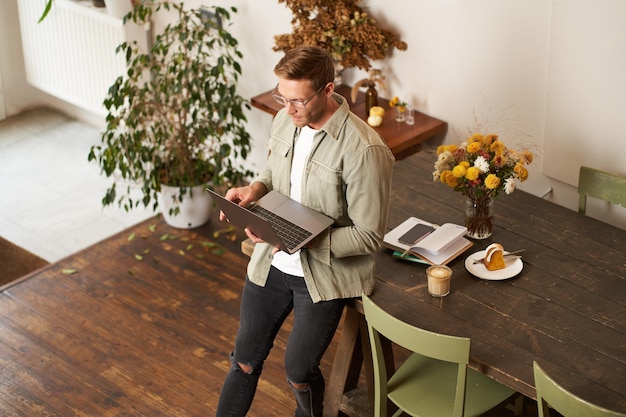 Afbeelding van een jonge succesvolle zakenman die op een tafel zit en naar een laptop kijkt die in een kantoor werkt