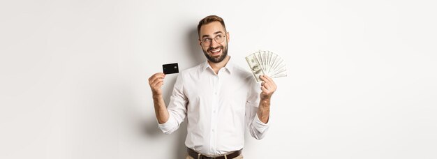 Afbeelding van een jonge zakenman die een creditcard en geld vasthoudt en naar de linkerbovenhoek kijkt en denkt a