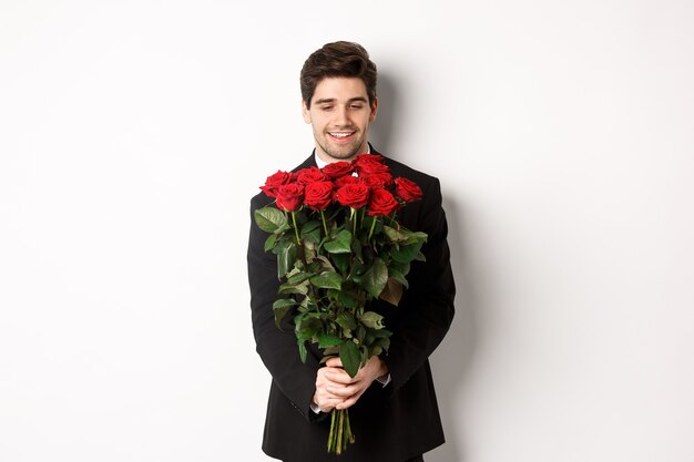 Afbeelding van een knappe vriend in een zwart pak, die een boeket rode rozen vasthoudt en glimlacht, op een date is, op een witte achtergrond staat