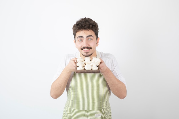 Afbeelding van een mannelijke kok die een bord met rauwe champignons op wit vasthoudt