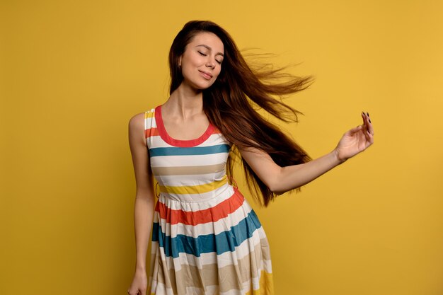 Afbeelding van een mooie glimlachende jonge vrouw in lichte zomerjurk geïsoleerd over gele muur. Mode portret van mooi meisje poseren met plezier over kleurrijke muur