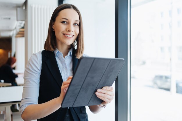 Afbeelding van een mooie jonge vrouw zitten terwijl ze een digitale tablet in haar handen houdt. Bedrijfseigenaar, cafetaria, restaurant