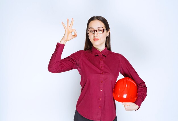 Afbeelding van een mooie vrouw met een bril die een crashhelm vasthoudt en een goed gebaar toont.