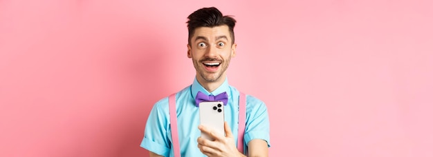Gratis foto afbeelding van een opgewonden man die promo-aanbieding online bekijkt terwijl hij een smartphone vasthoudt en verbaasd naar de camera staart