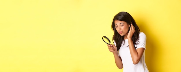 Gratis foto afbeelding van een schattige afro-amerikaanse vrouw die op zoek is naar iets met een vergrootglas dat naar beneden kijkt