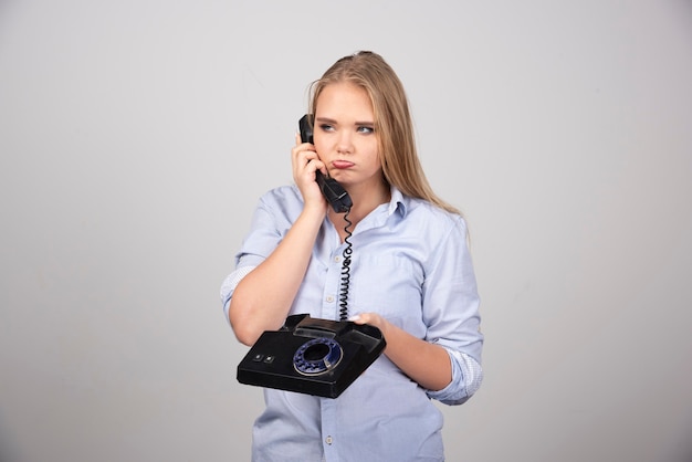 Afbeelding van een schattige jonge vrouw met een zwarte oude handset die op haar wangen blaast