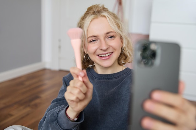 Afbeelding van een stijlvolle jonge vrouw, een social media influencer, die foto's maakt met haar mobiele telefoon terwijl ze make-up maakt.